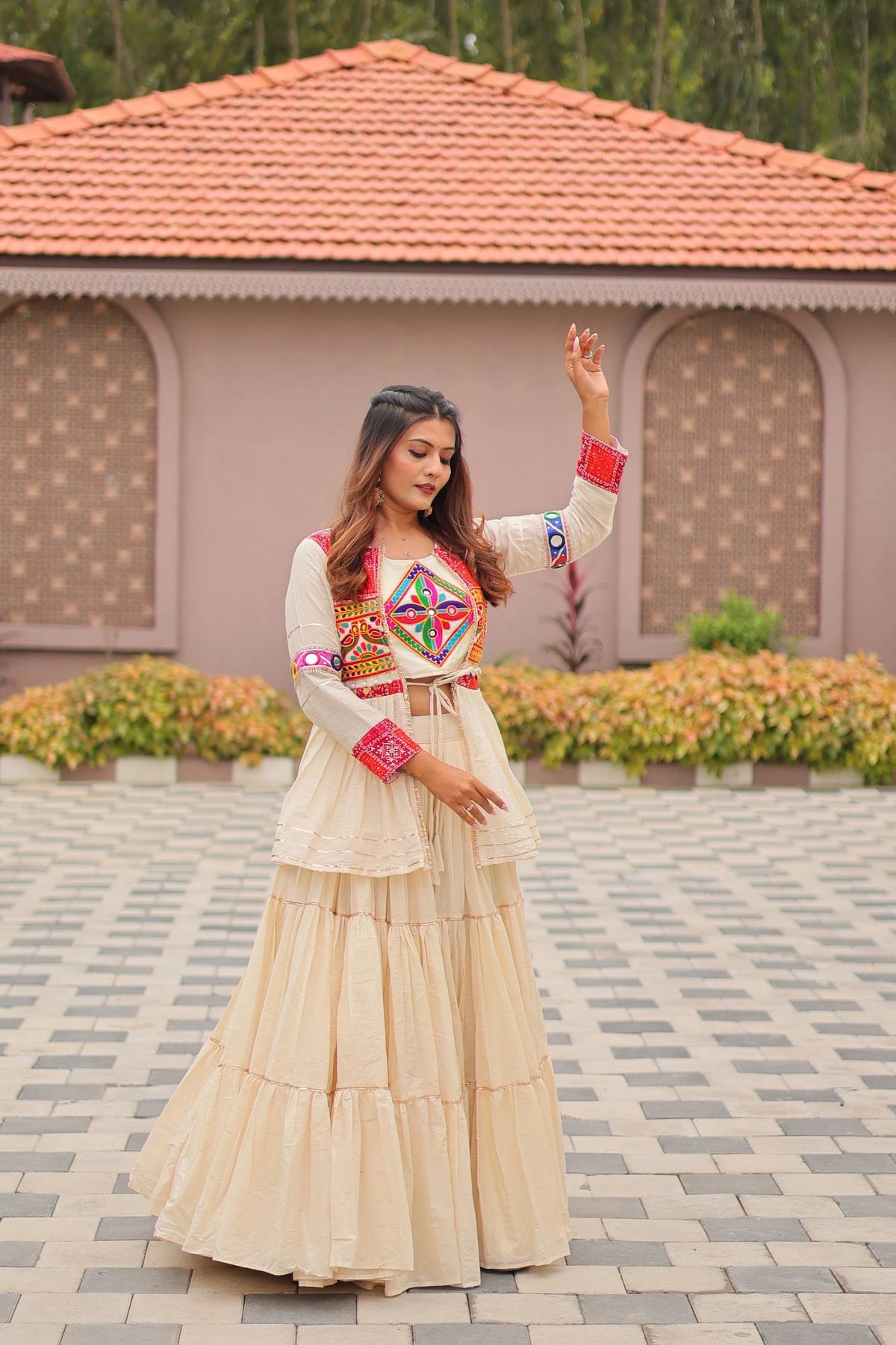 Woman in traditional outfit standing outdoors with a building and greenery in the background