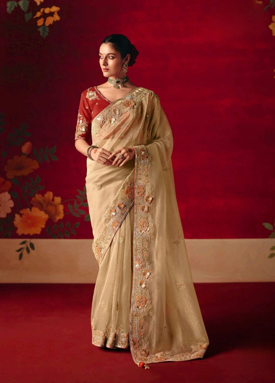 Woman in a beige saree with floral patterns against a red background