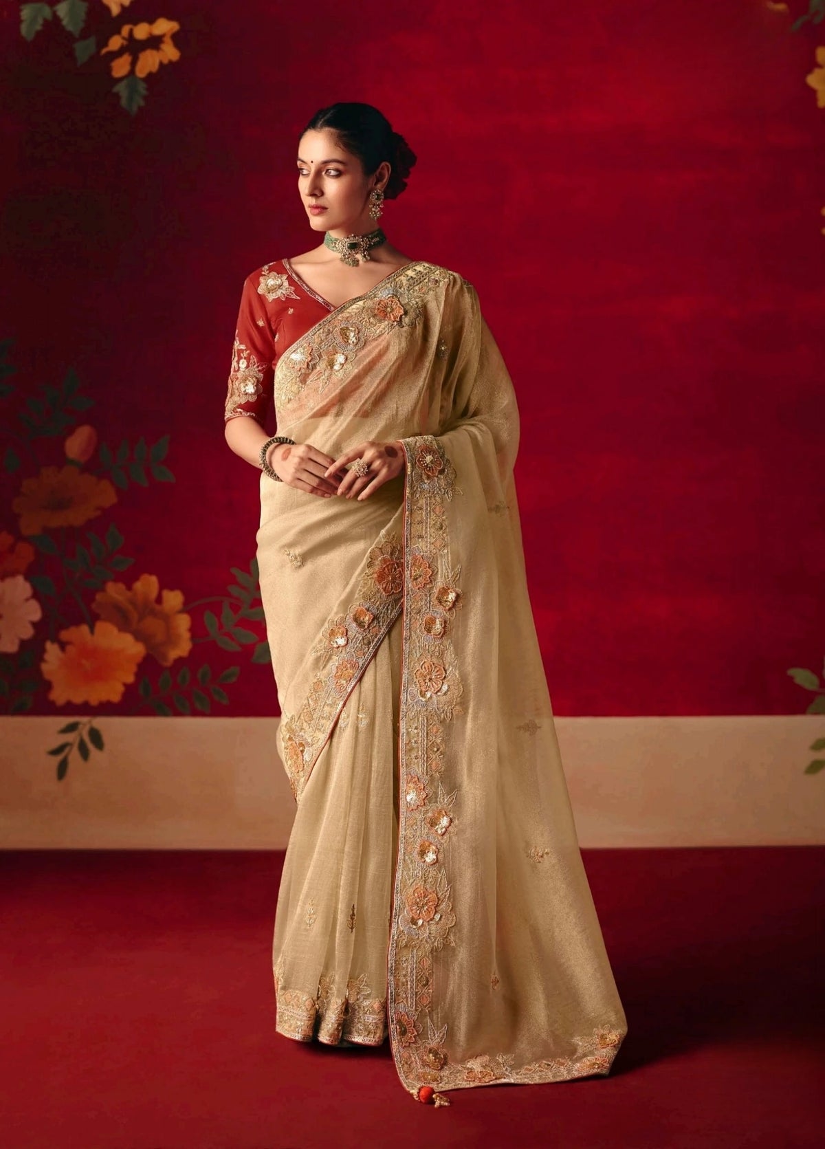 Woman in a beige saree with floral patterns against a red background