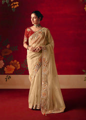 Woman in a beige saree with floral patterns against a red background