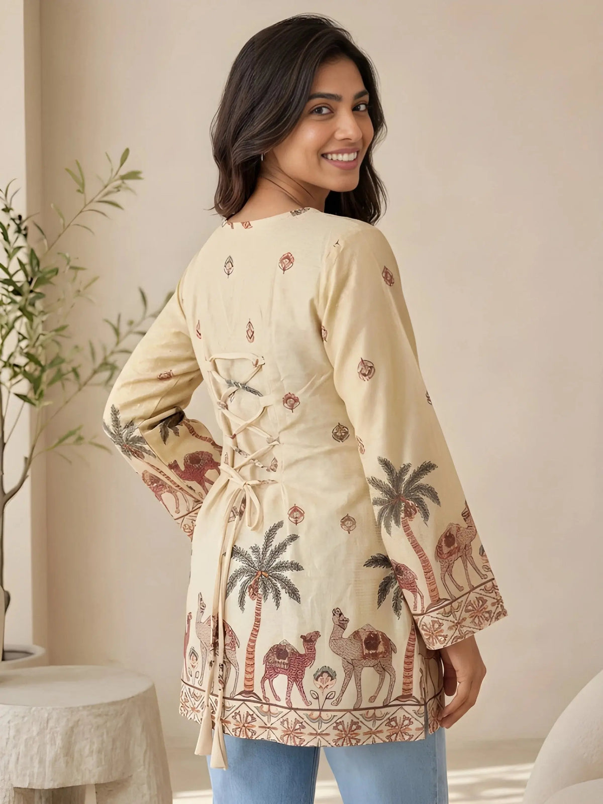 Woman wearing a beige patterned dress with palm trees and camels in a room setting.