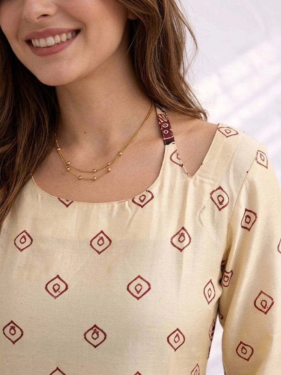 Woman wearing a cream-colored top with red geometric patterns and a gold necklace.