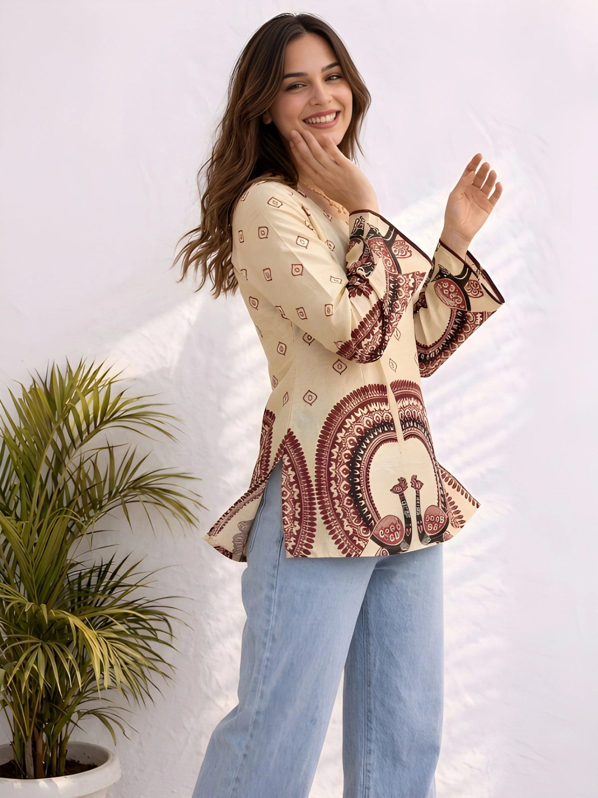 A woman smiles while wearing a cream printed long-sleeve top with light blue wide-leg jeans
