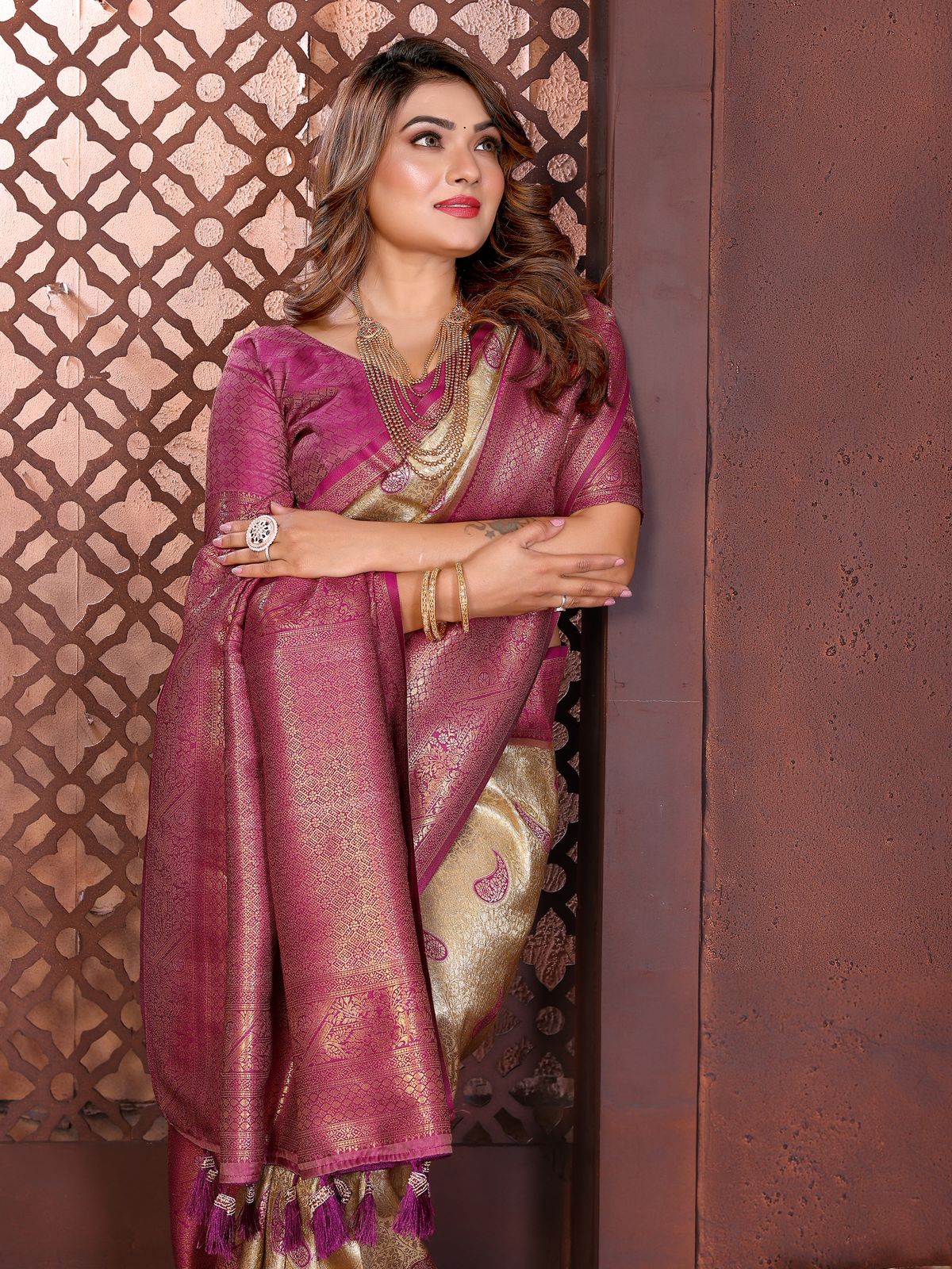 Woman in a traditional pink saree with gold patterns against an ornate wall.