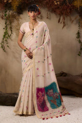 The saree has subtle pastel patterns and a bold floral accent near the pallu edge.

