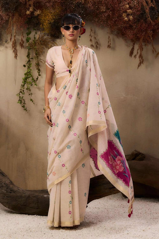 A woman stands elegantly wearing a soft blush pink saree with delicate floral embroidery