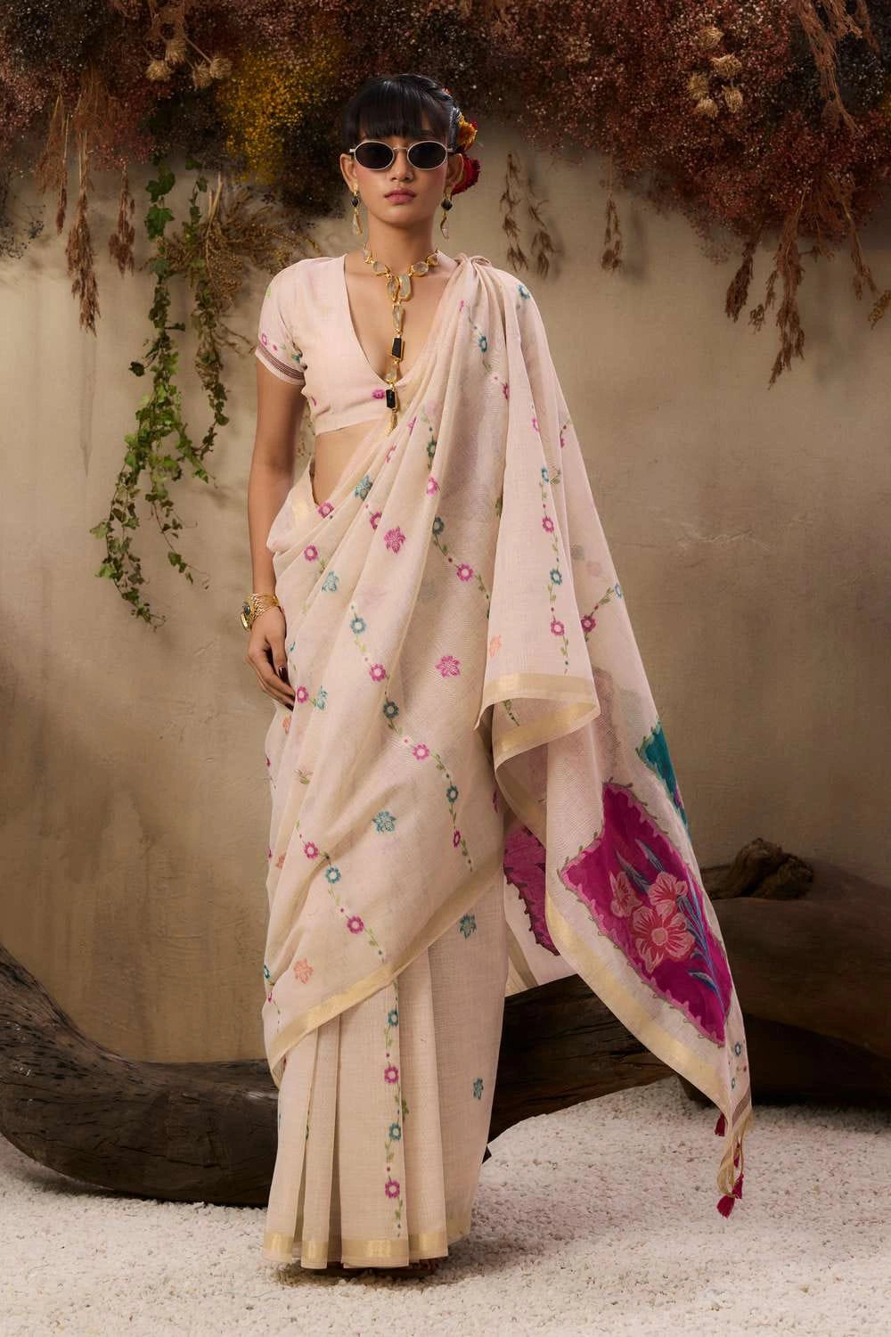A woman stands elegantly wearing a soft blush pink saree with delicate floral embroidery