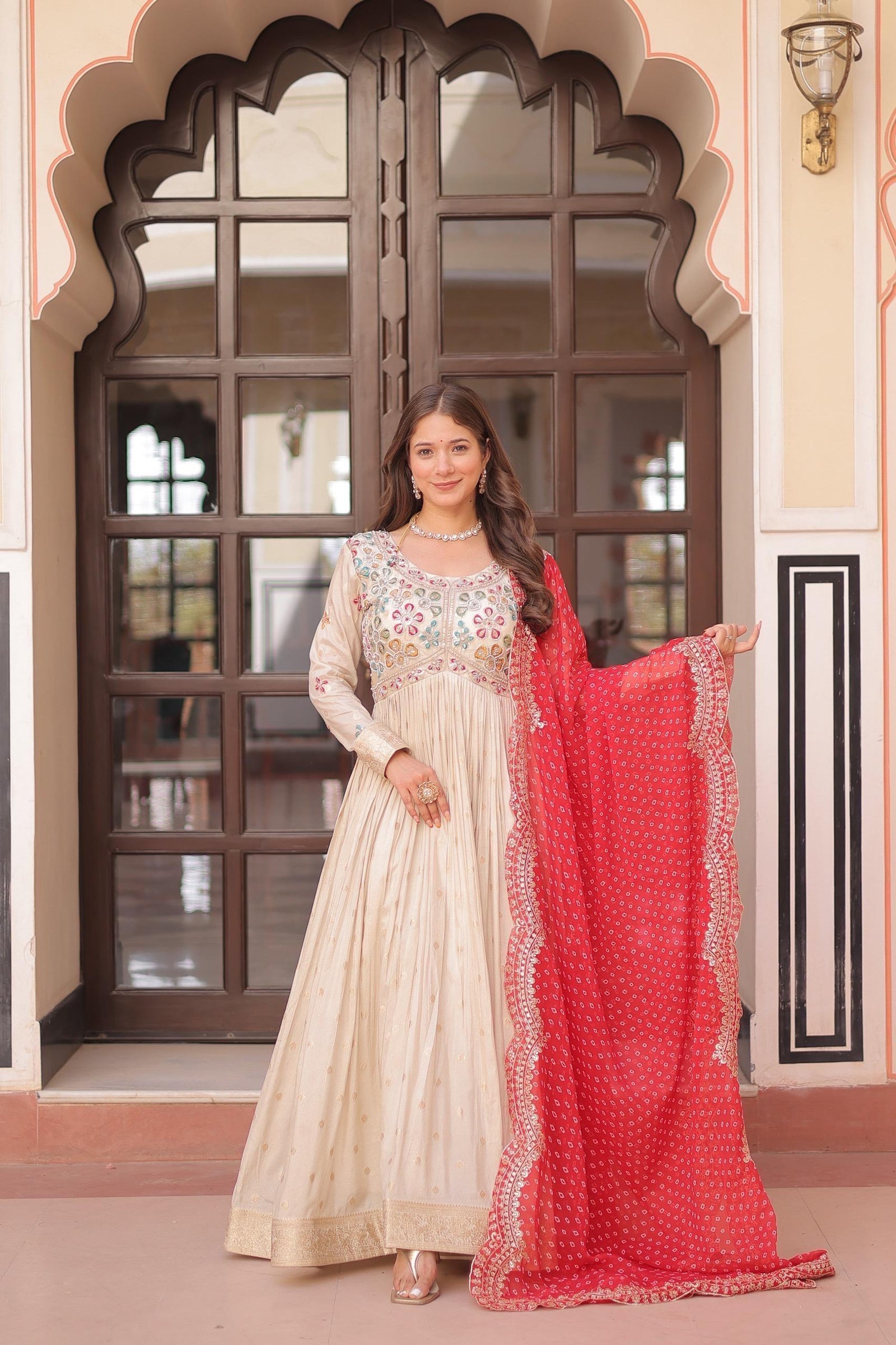 Woman in traditional outfit with a red dupatta standing in front of an ornate doorway.