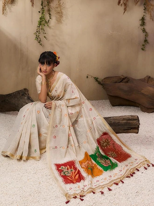 A woman stands elegantly in a soft pastel pink saree with delicate floral embroidery and printed motifs.
