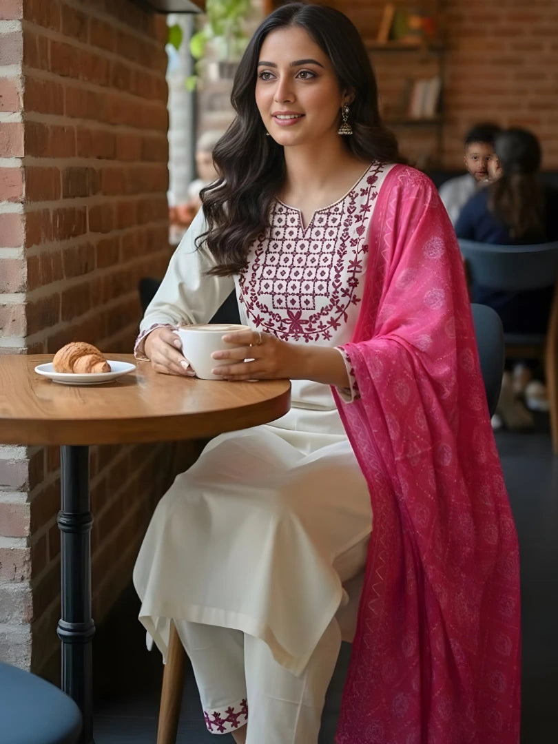 Woman sitting at a table in a cafe holding a cup, wearing a traditional outfit with a pink dupatta.