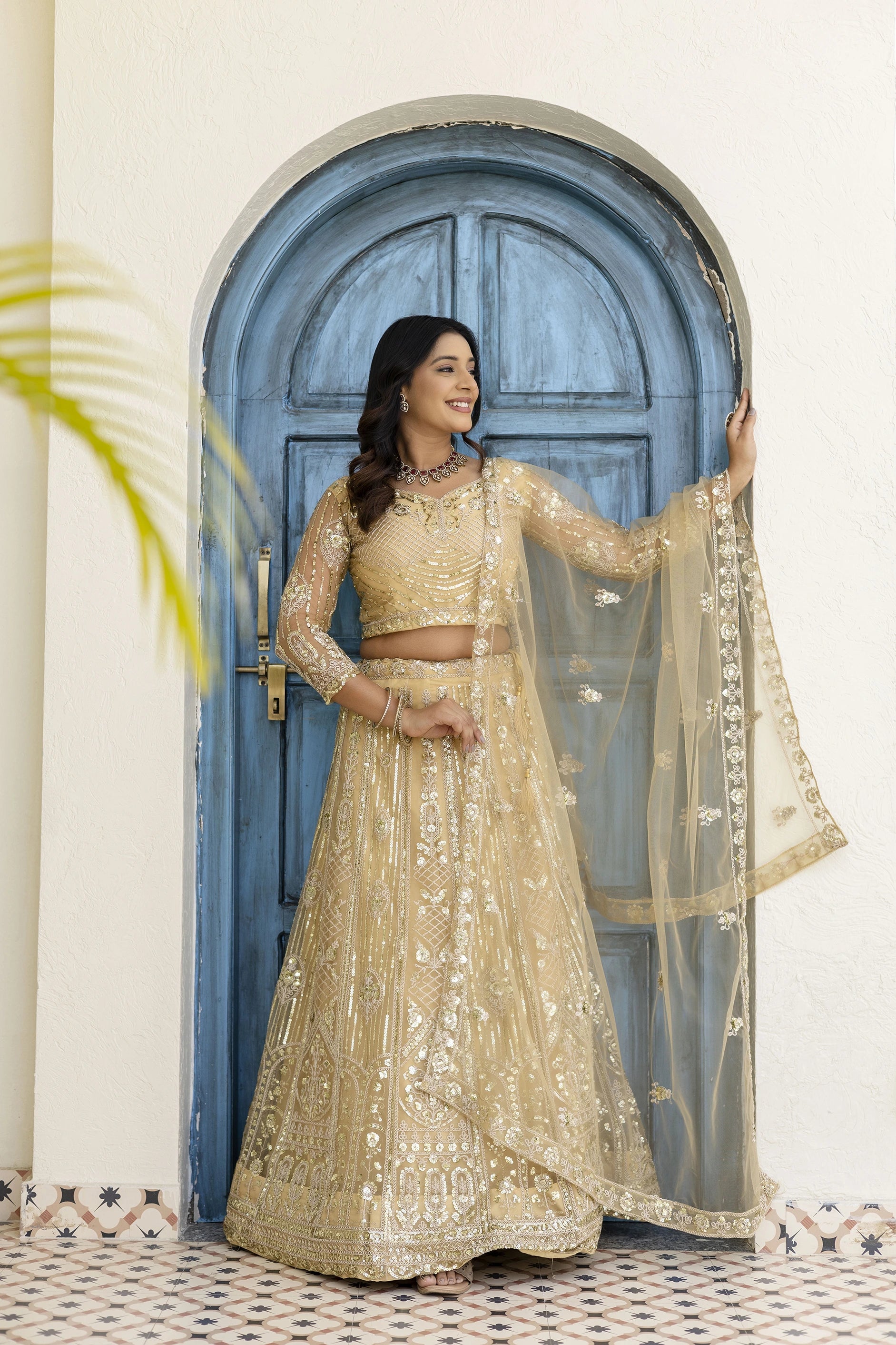 Woman in a gold embroidered traditional outfit standing in front of a blue door.