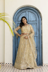 Woman in a beige embroidered lehenga standing in front of a blue door.