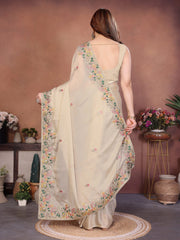 Woman wearing a light-colored saree with floral patterns in an indoor setting.