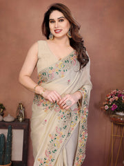 Woman wearing a beige saree with floral patterns against a brown background