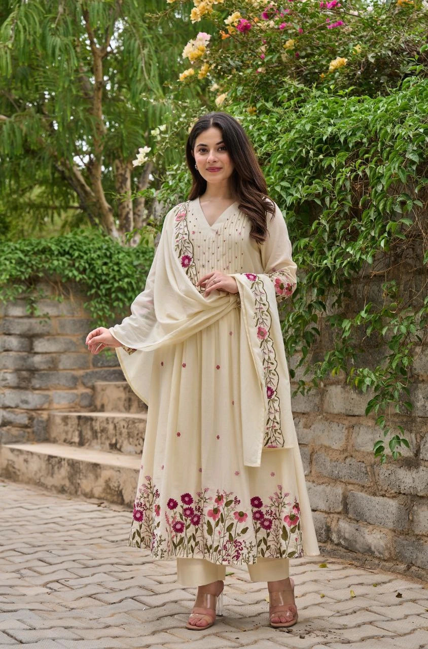 Woman in a cream-colored traditional outfit with floral patterns standing outdoors.