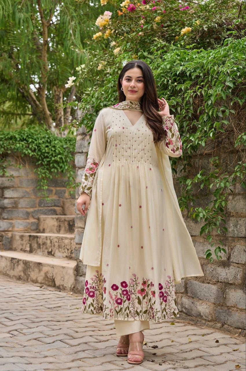 Woman in a cream-colored traditional outfit with floral patterns standing outdoors.