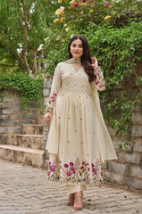 Woman in a cream-colored traditional outfit with floral patterns standing outdoors.