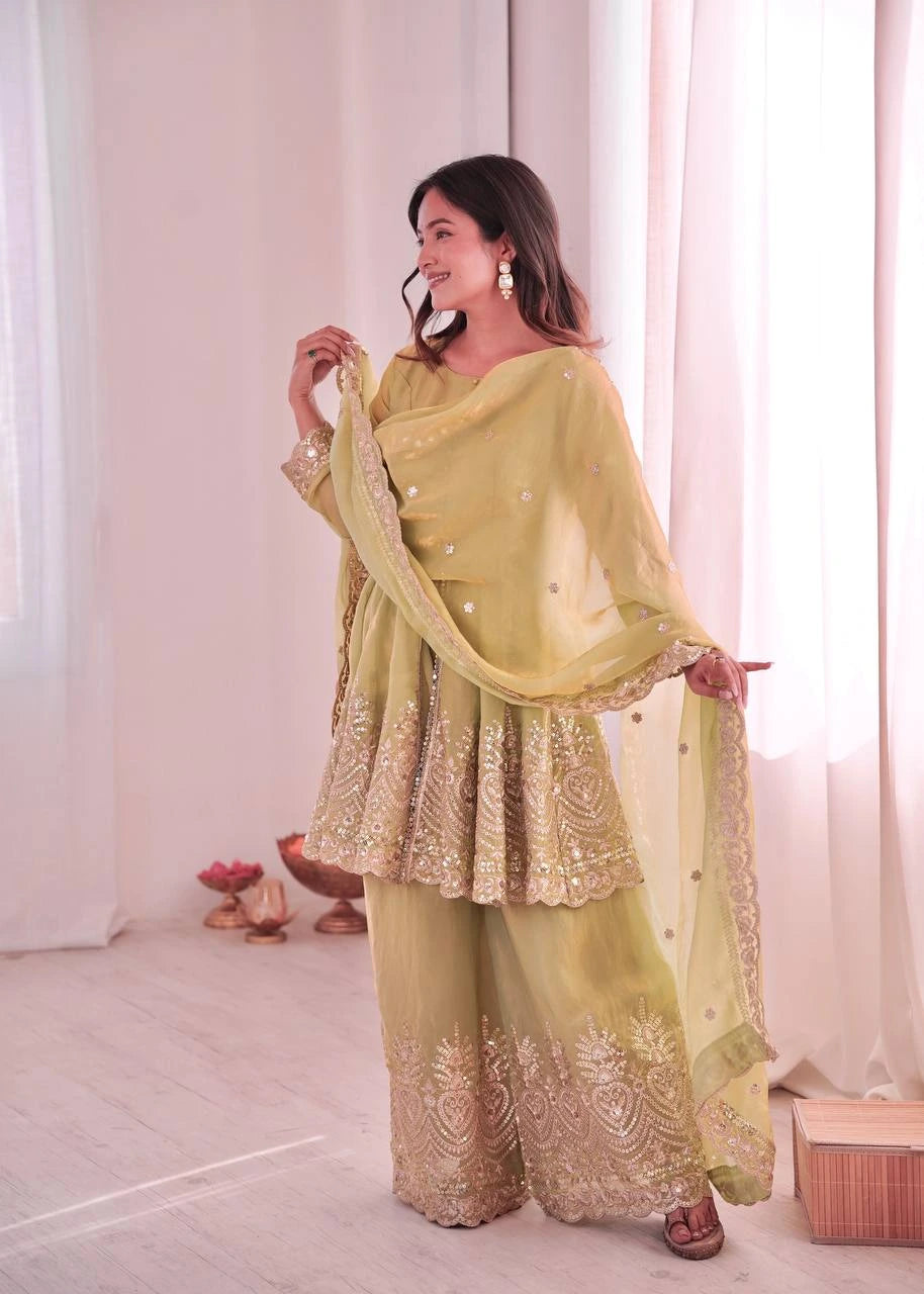 Woman in a light green traditional outfit with embroidery, standing against a white curtain background.