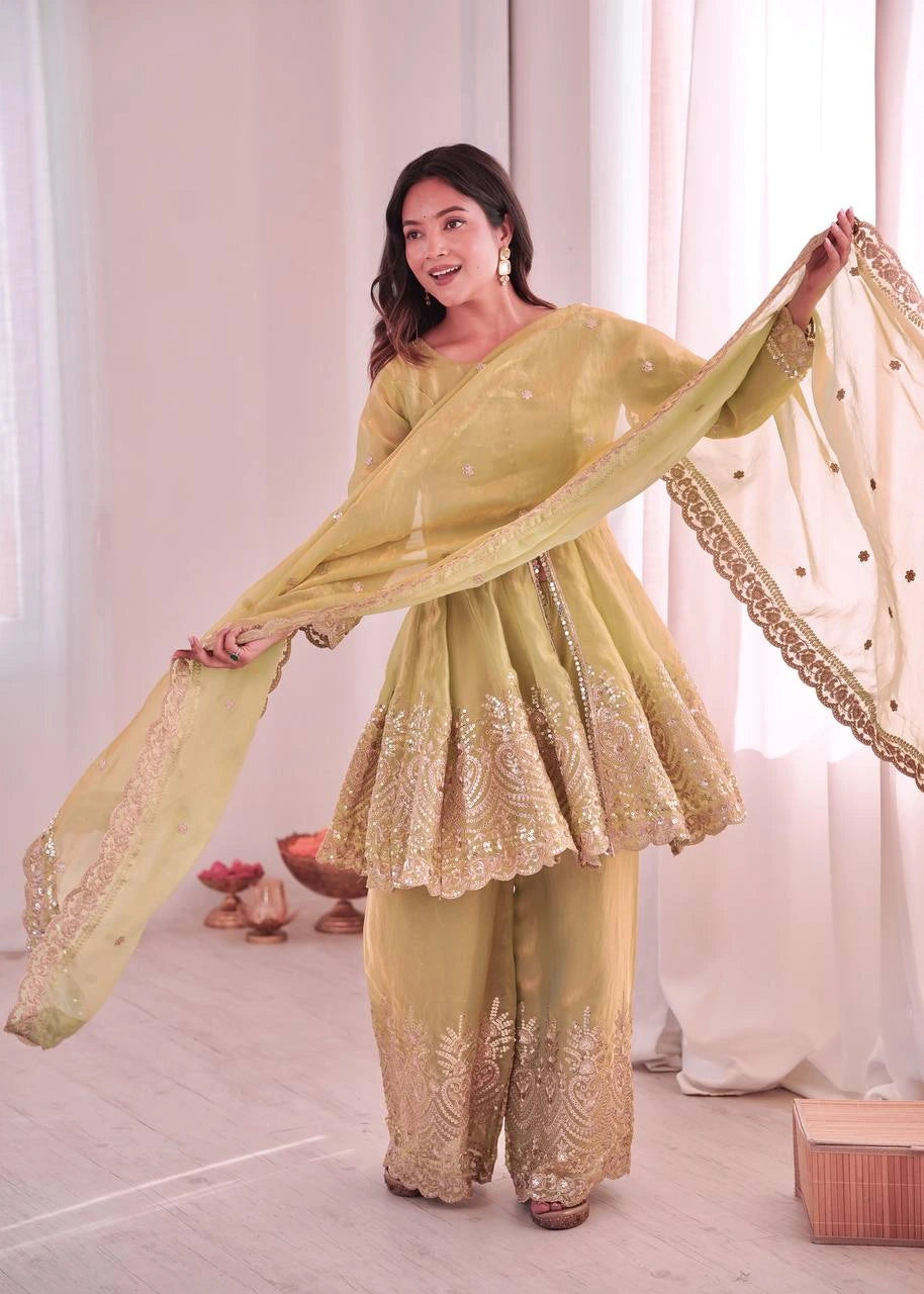Woman in a light green traditional outfit with a sheer dupatta, standing indoors.