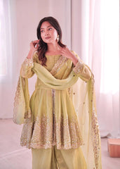 Woman wearing a light green traditional outfit with embroidery in a softly lit room.