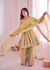 Woman in a light green traditional outfit with a sheer dupatta, standing indoors.