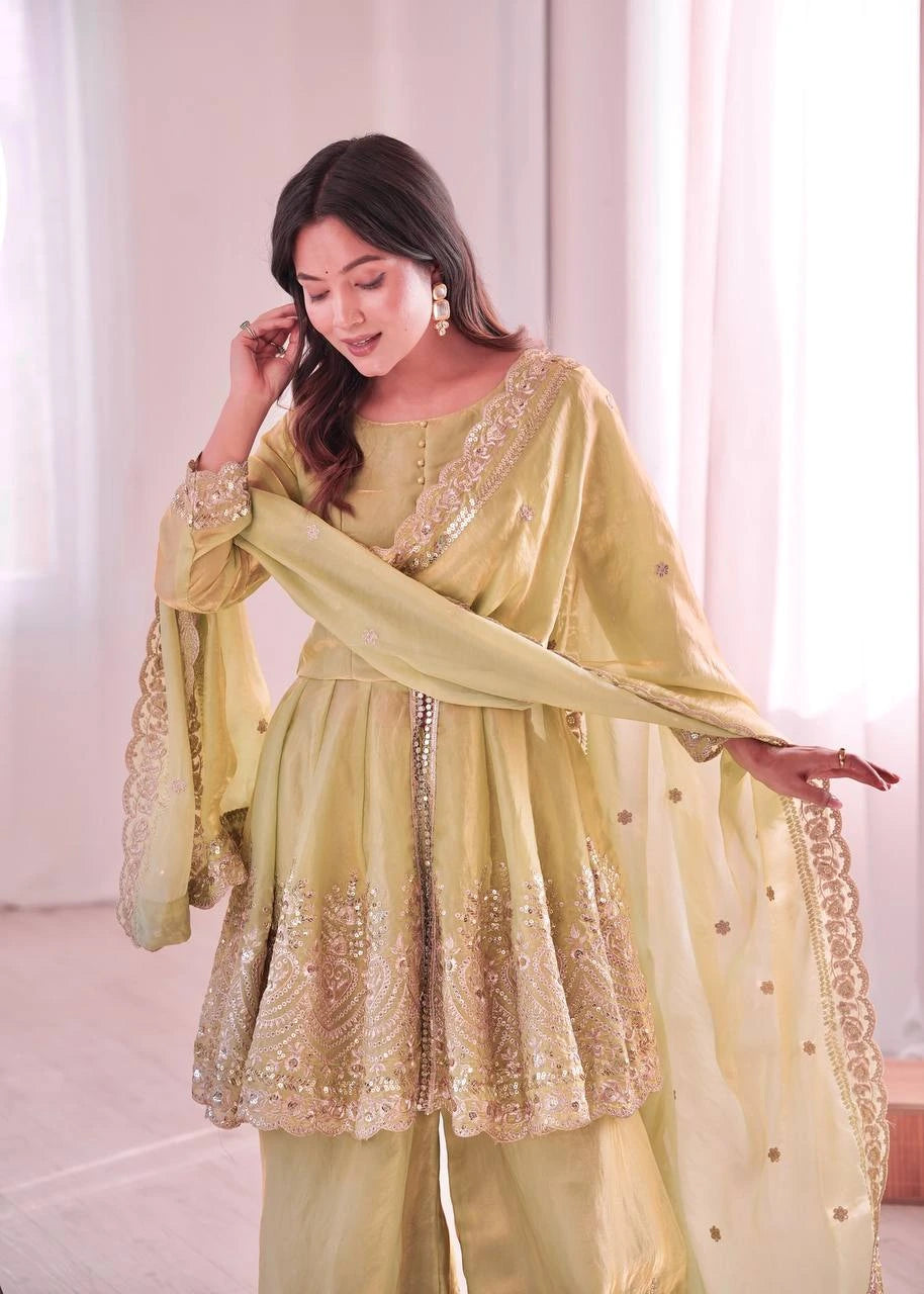 Woman wearing a light green traditional outfit with gold embroidery in a bright room.