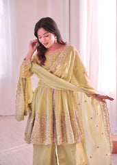 Woman wearing a light green traditional outfit with gold embroidery in a bright room.