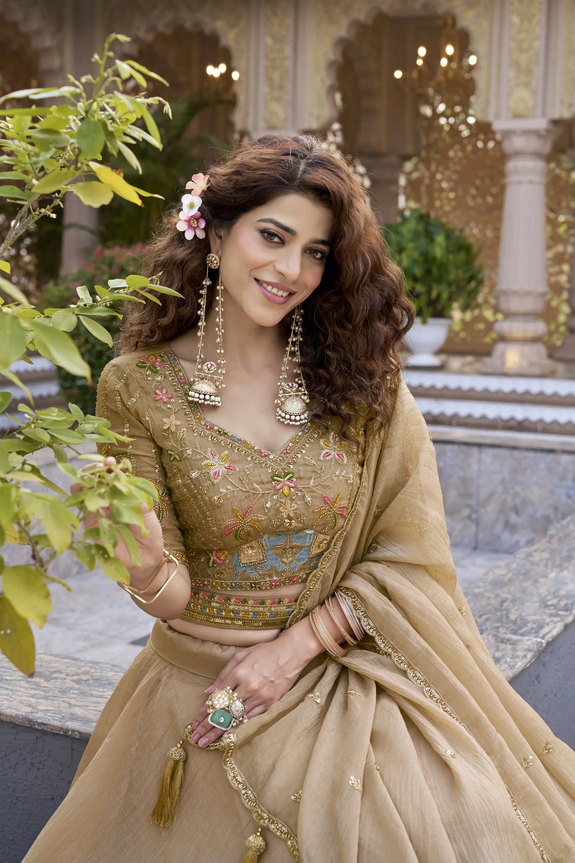 Woman in traditional embroidered outfit with jewelry, standing in a decorative indoor setting.
