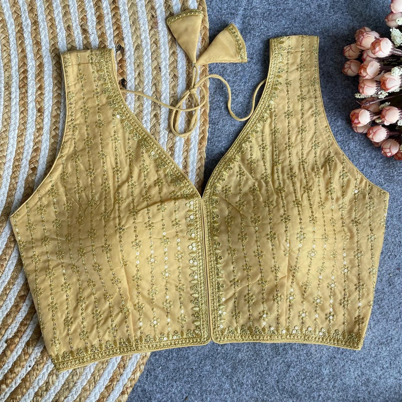Gold embroidered top on a textured surface with flowers in the background