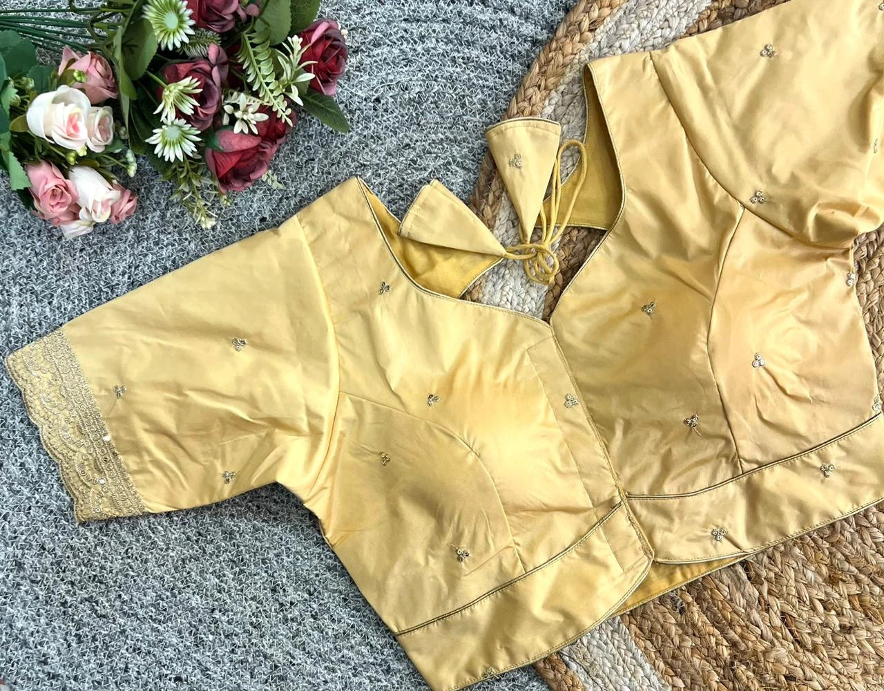 Gold blouse with decorative elements on a textured surface with flowers.