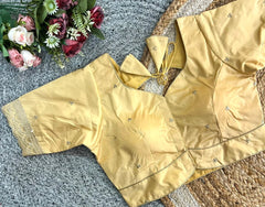 Gold blouse with decorative elements on a textured surface with flowers.