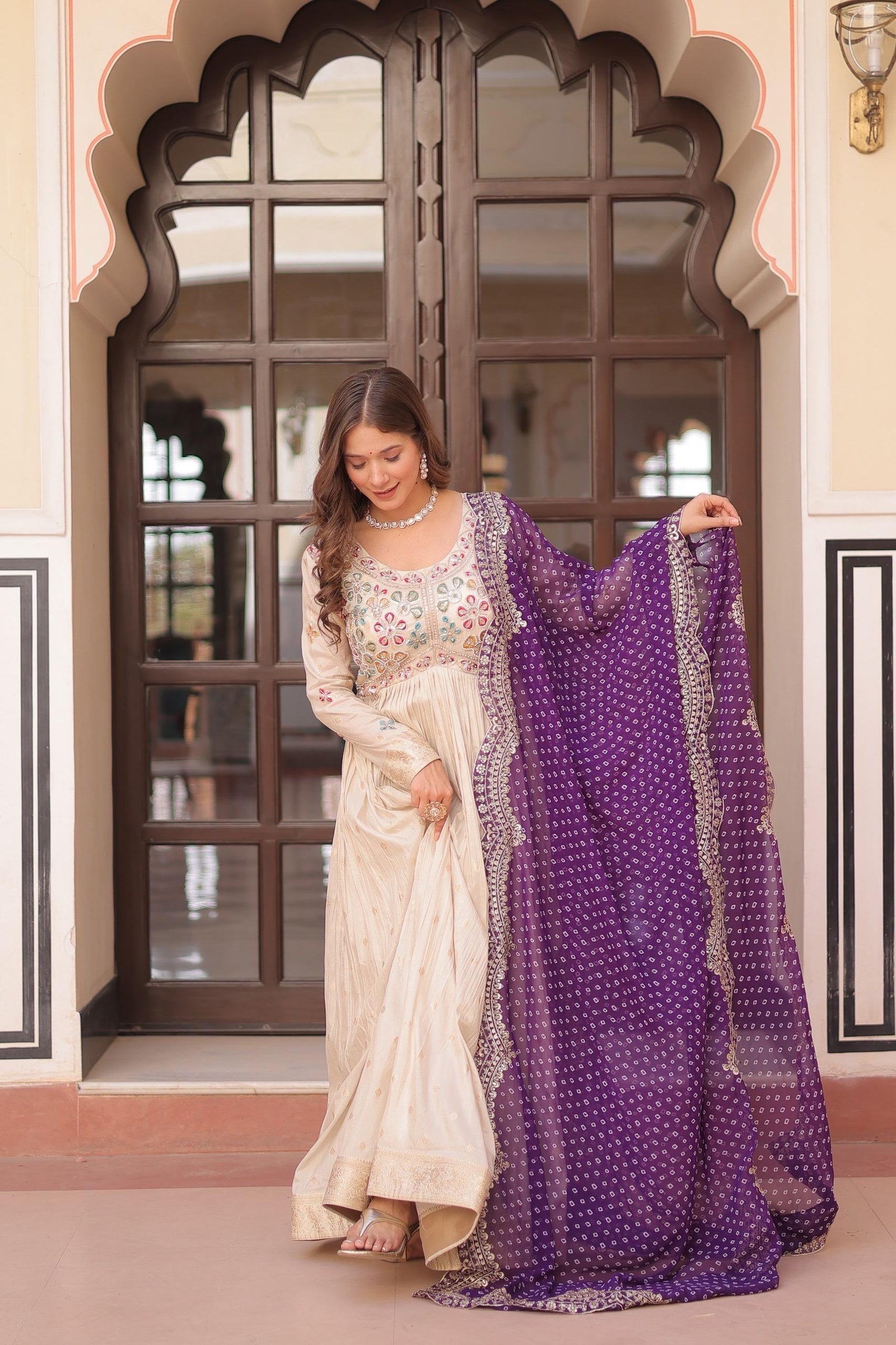 Woman holding a white and purple saree in front of an ornate door.
