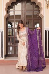 Woman holding a white and purple saree in front of an ornate door.