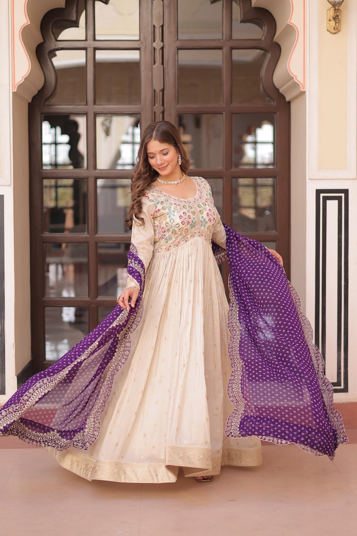 Woman in a traditional outfit with a purple dupatta standing in front of a decorative door.