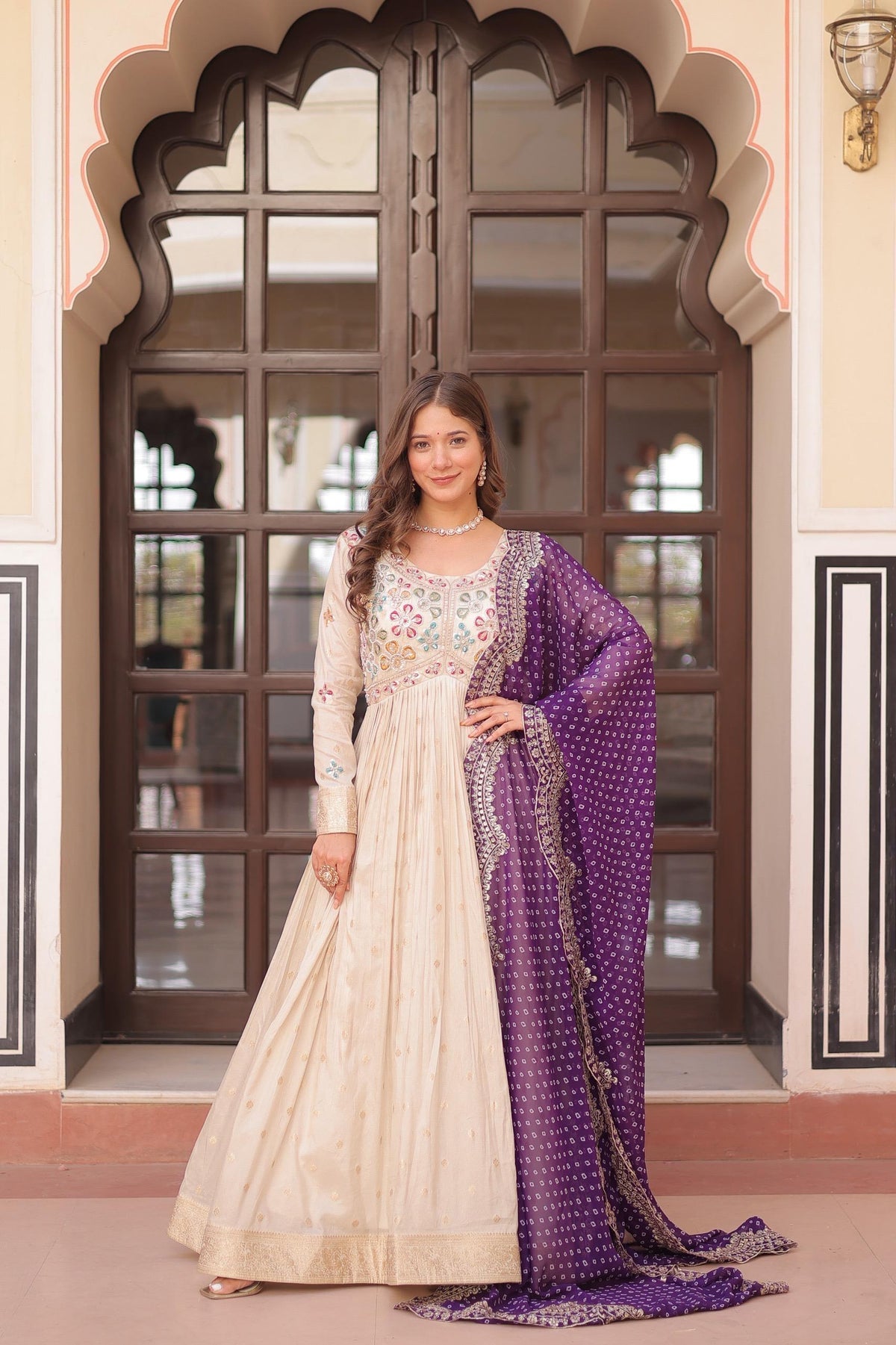 Woman in a traditional outfit with a purple dupatta standing in front of an ornate door.
