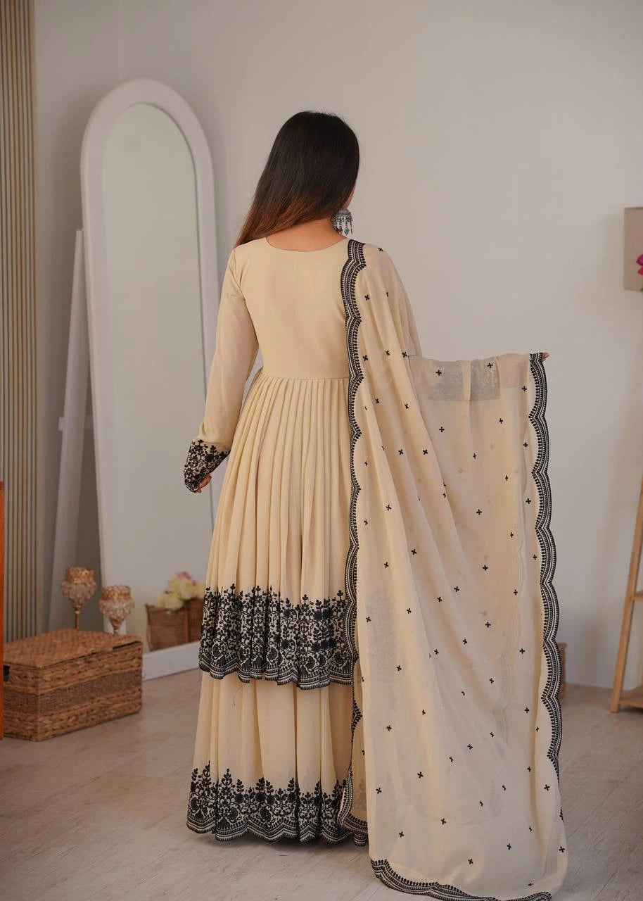 Woman in a beige dress with black embroidery holding a matching dupatta in a room.