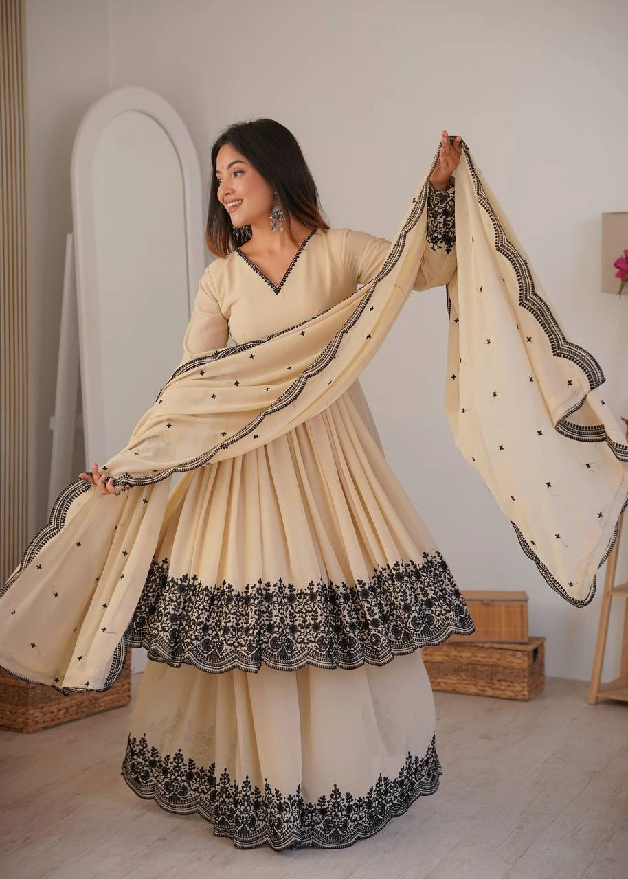 Woman in a beige traditional outfit with black embroidery holding a matching dupatta.