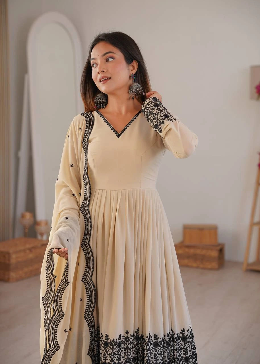 Woman wearing a beige dress with black embroidery in a room setting.