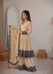 Woman in a beige and black traditional outfit holding a matching dupatta in a room.