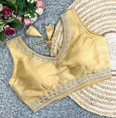 Gold blouse with intricate lace detailing on a textured surface with flowers.