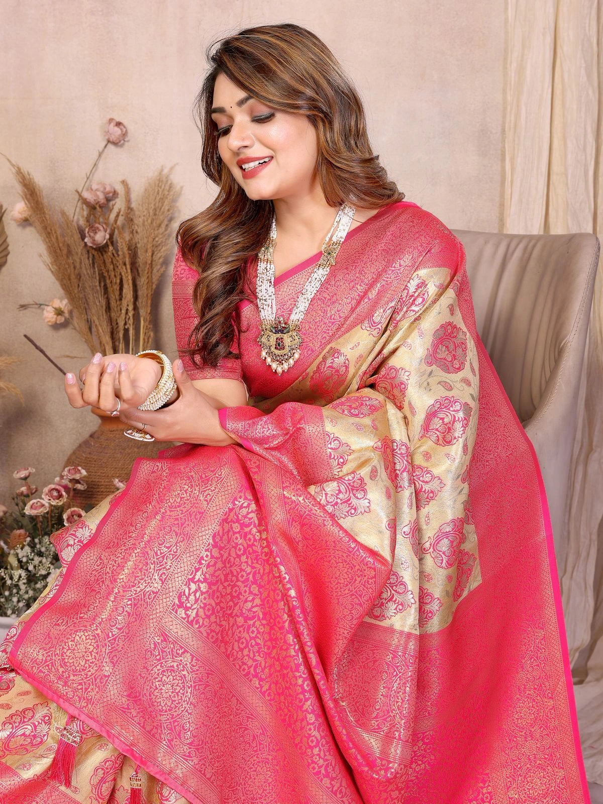 Woman in a pink saree with gold patterns sitting on a couch.