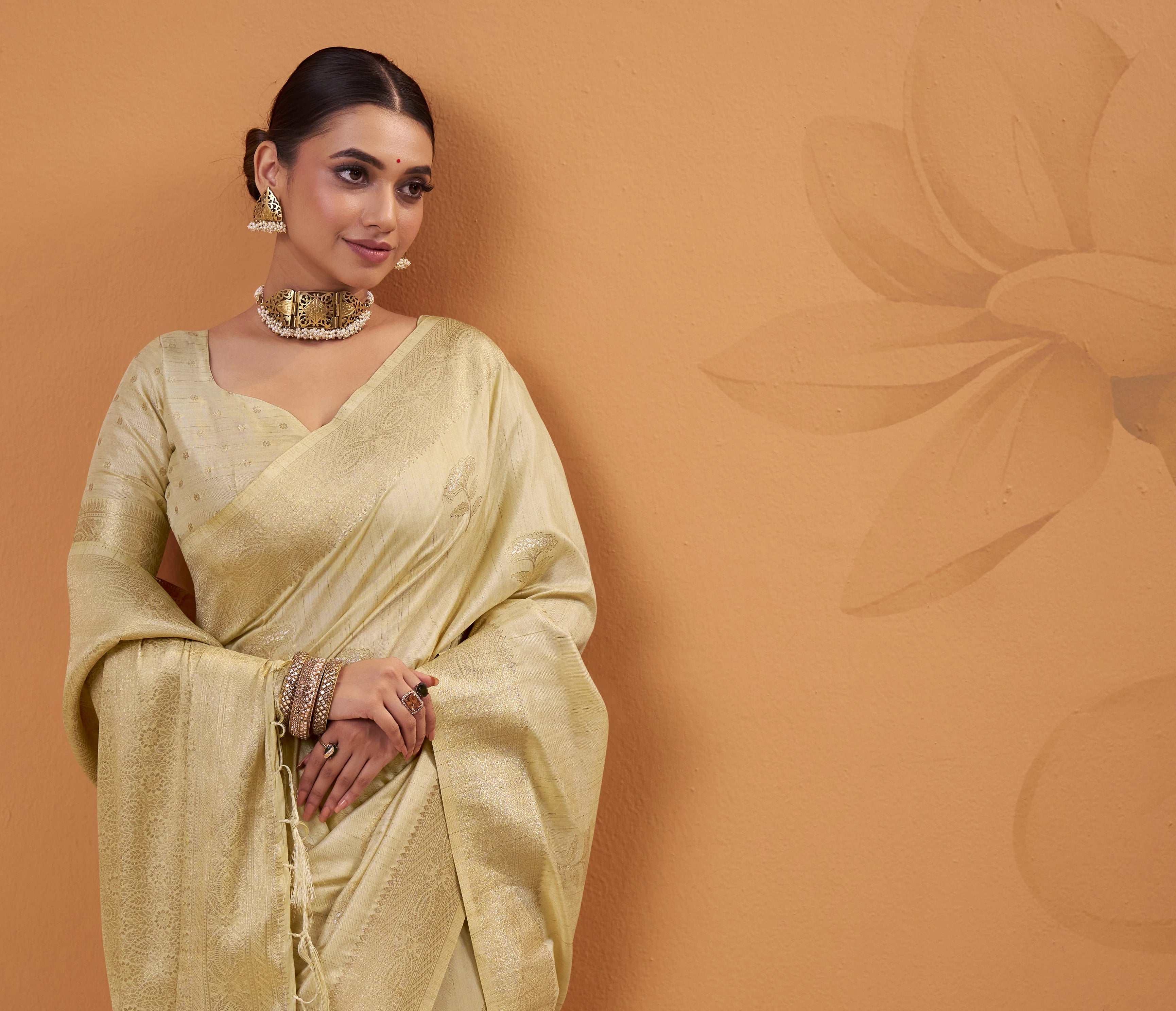 Woman in a light yellow saree against a brown background