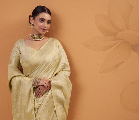 Woman in a light yellow saree against a brown background