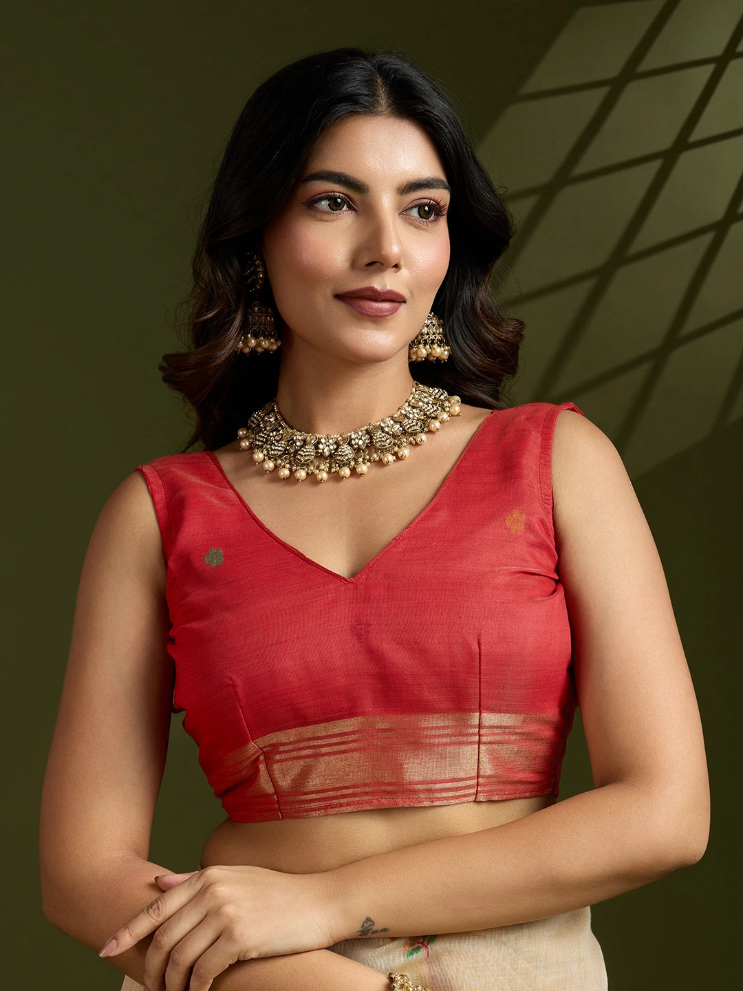 Woman wearing a red blouse with gold jewelry against a dark background
