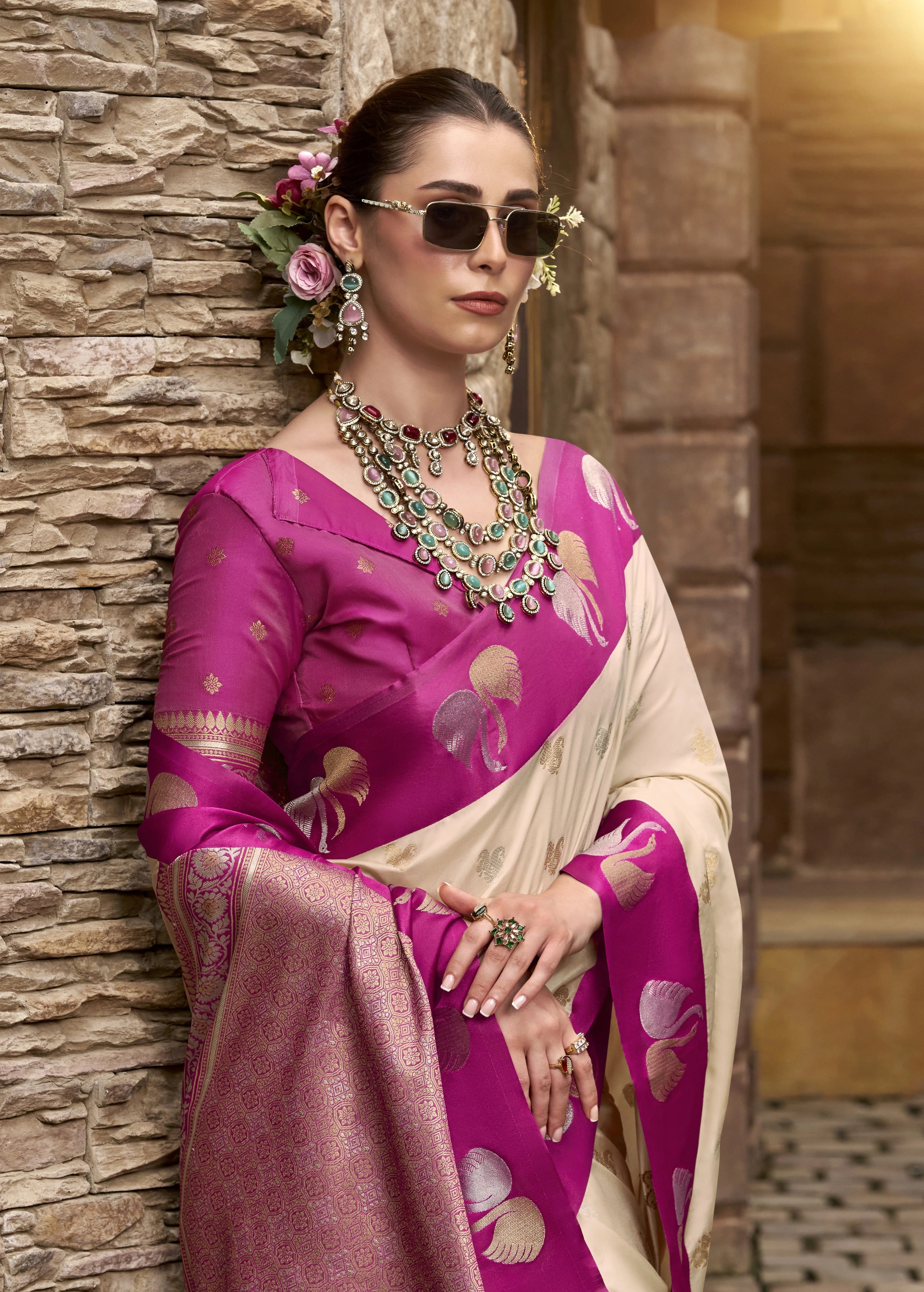 Woman in a pink saree with floral decorations against a stone wall.