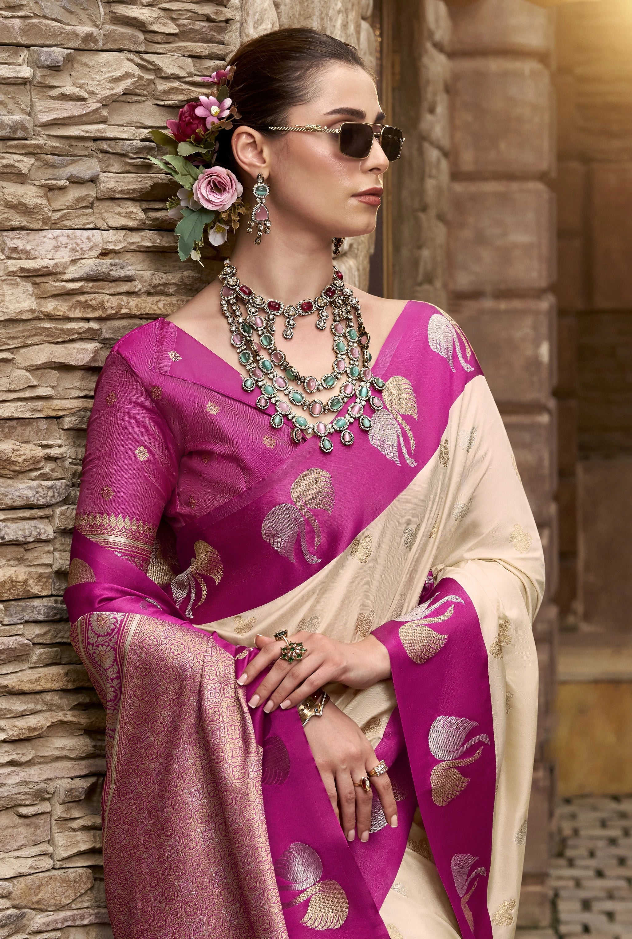 Woman in a pink saree with gold patterns against a stone wall.
