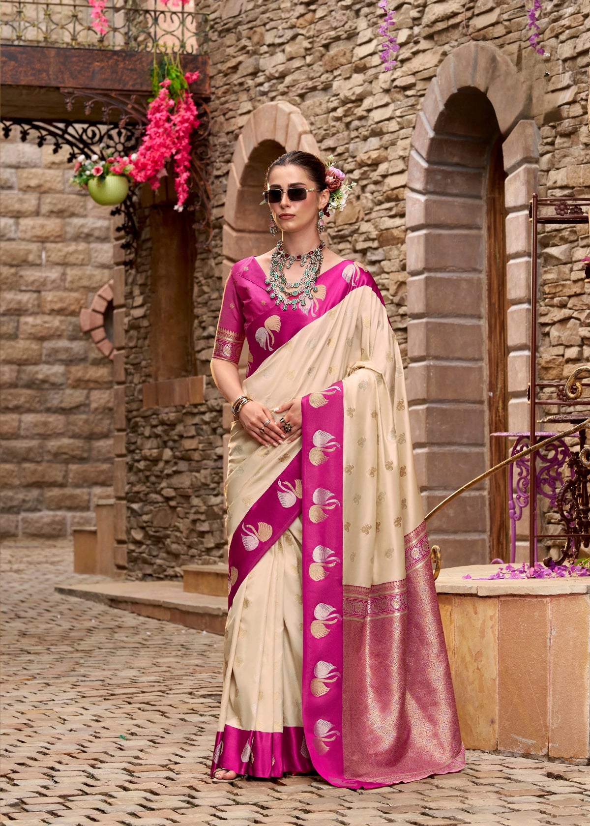 Woman in a pink and white saree standing in front of a stone building.