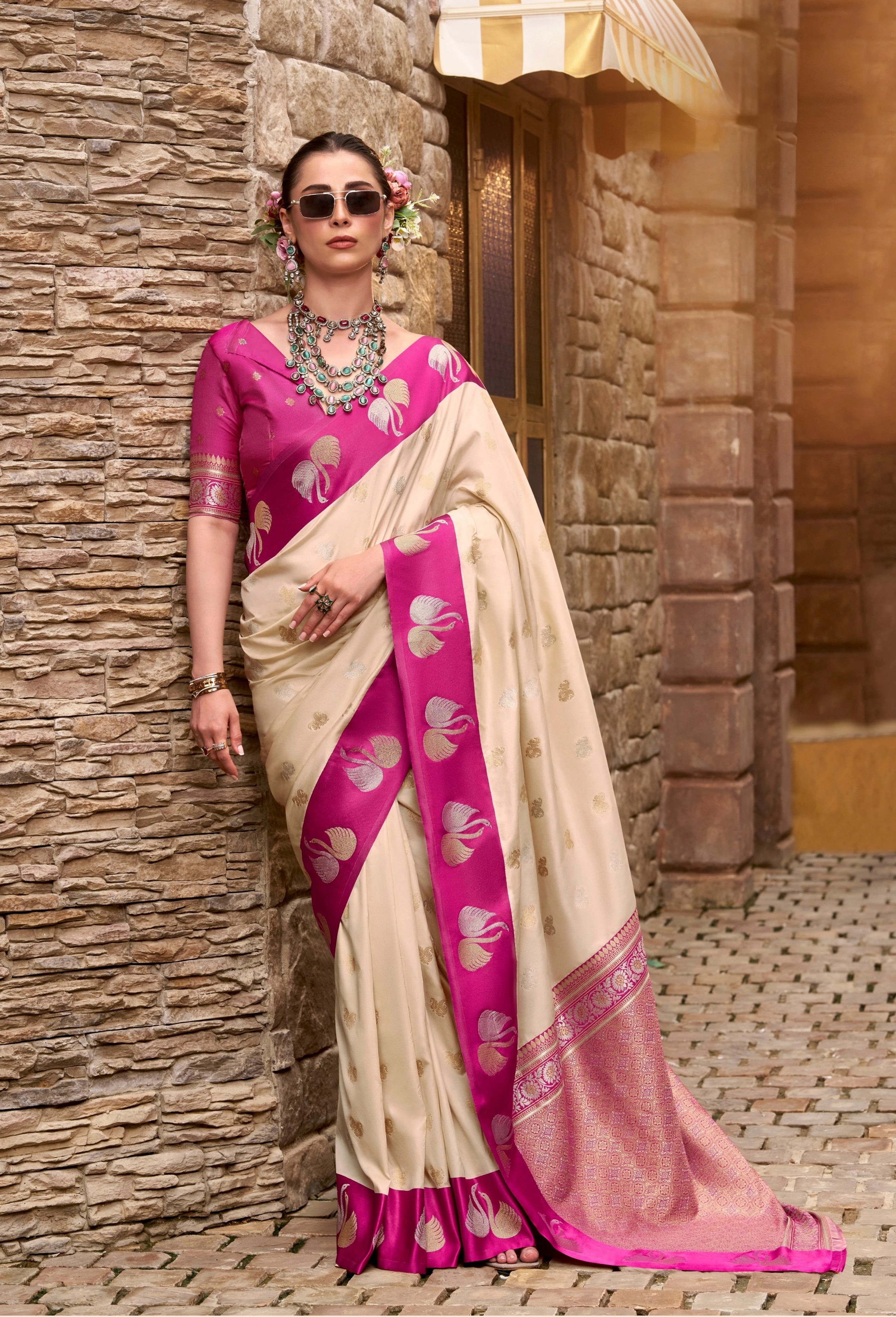 Woman wearing a pink and white saree against a stone wall.