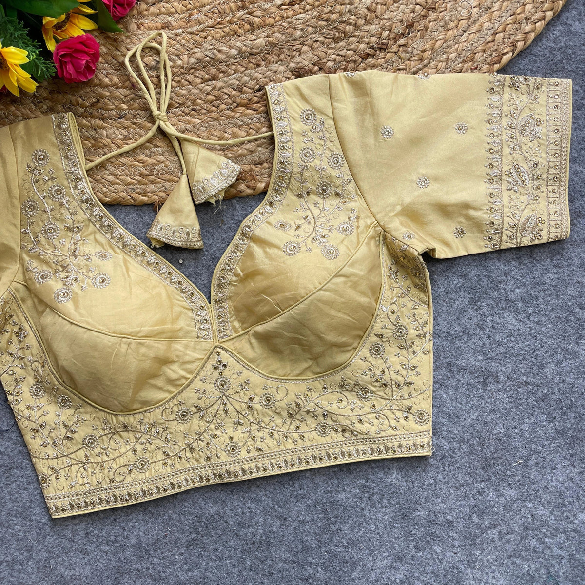 Gold embroidered blouse on a textured surface with flowers in the background