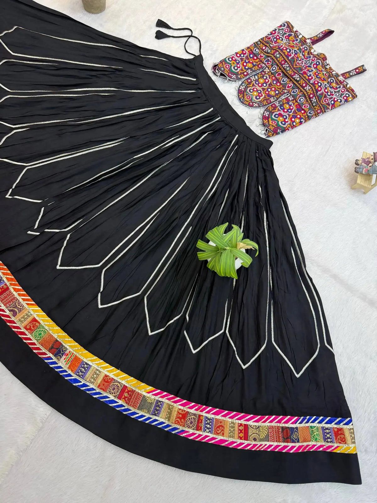 Flat lay detail of black circular lehenga skirt showing white chevron embroidery and colorful patola border